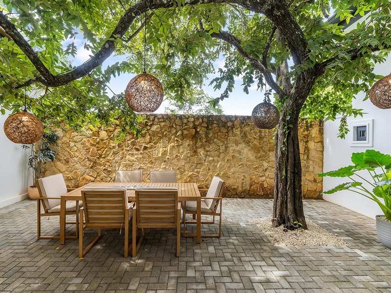 A walled courtyard with a mature tree, woven pendant lights and a teak dining table