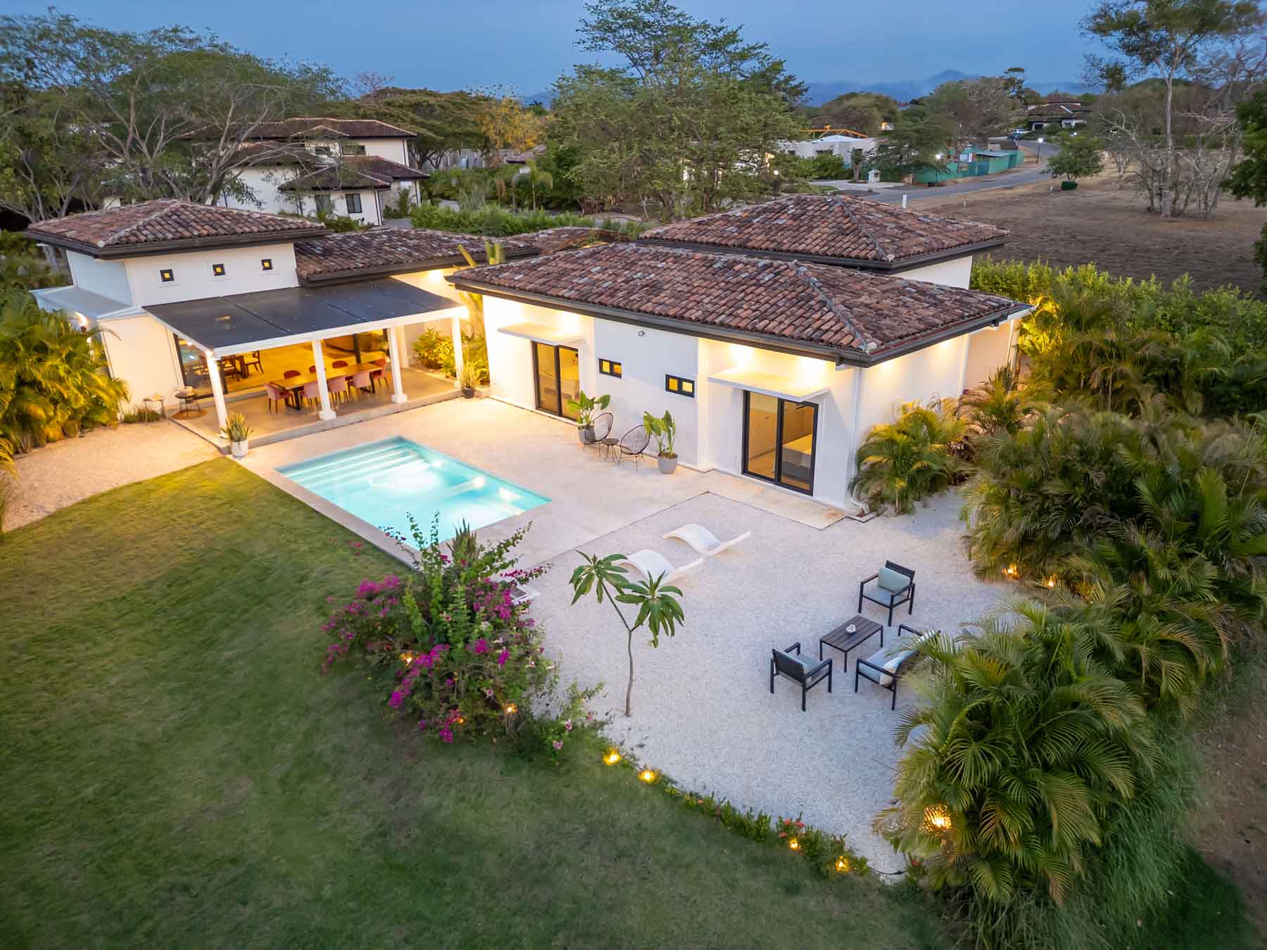 Casa Allamanda at dusk, seen from above: tiled roofs, a lit pool and a lawn edged with bougainvillea
